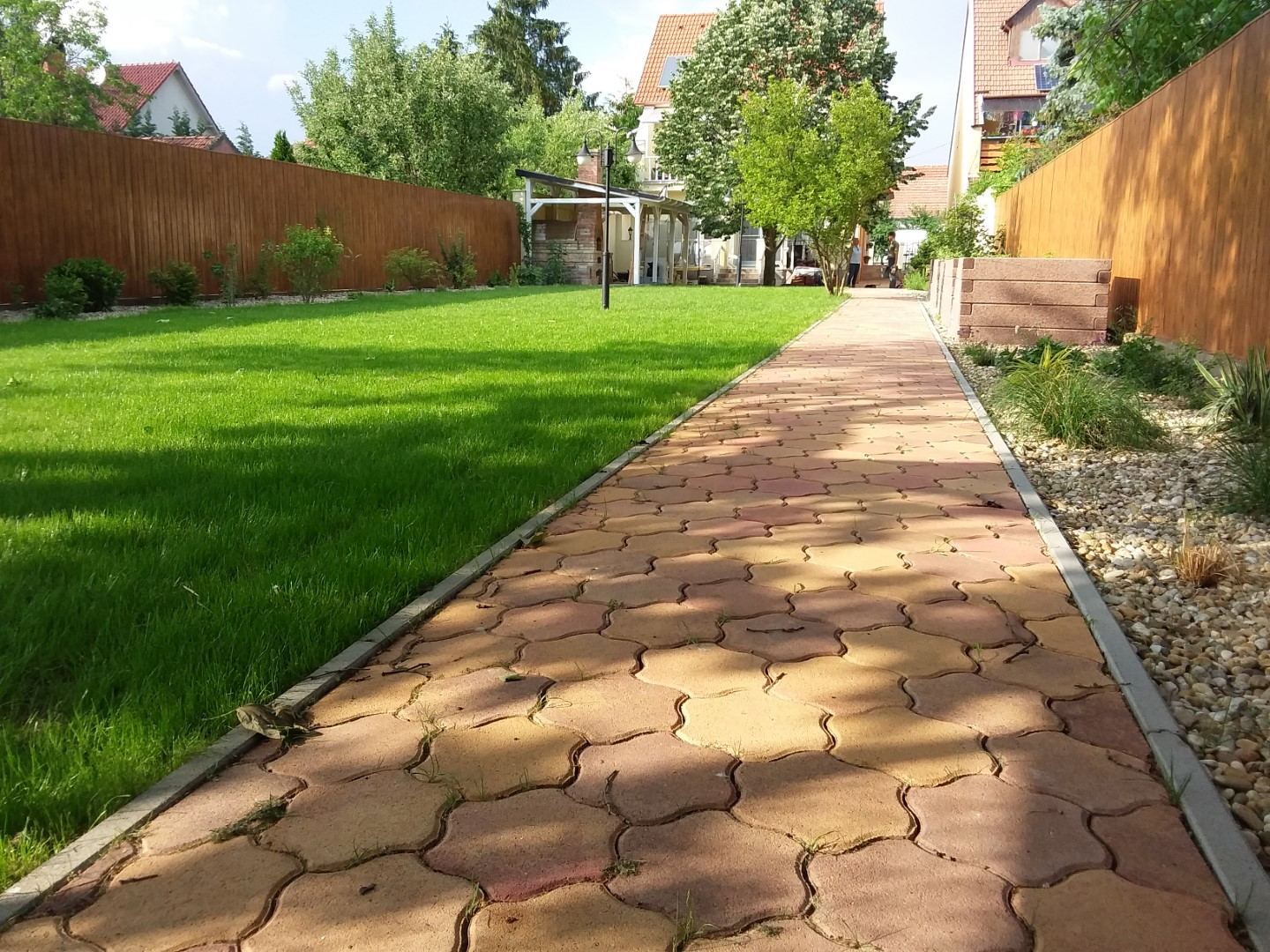 Hosszú térköves kerti út gondozott gyep és fák mellett